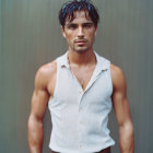 Young man in unbuttoned white sleeveless shirt with tousled hair against subdued backdrop