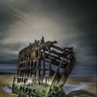 Weathered shipwreck onshore with colorful hull under dramatic sky