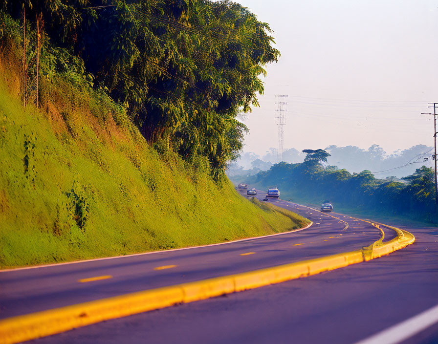 Curved Road with Yellow Lines, Grass Hill, and Vehicles in Hazy Sky