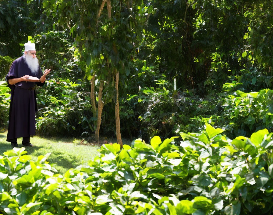 Bearded man in dark clothes reading book in lush green garden