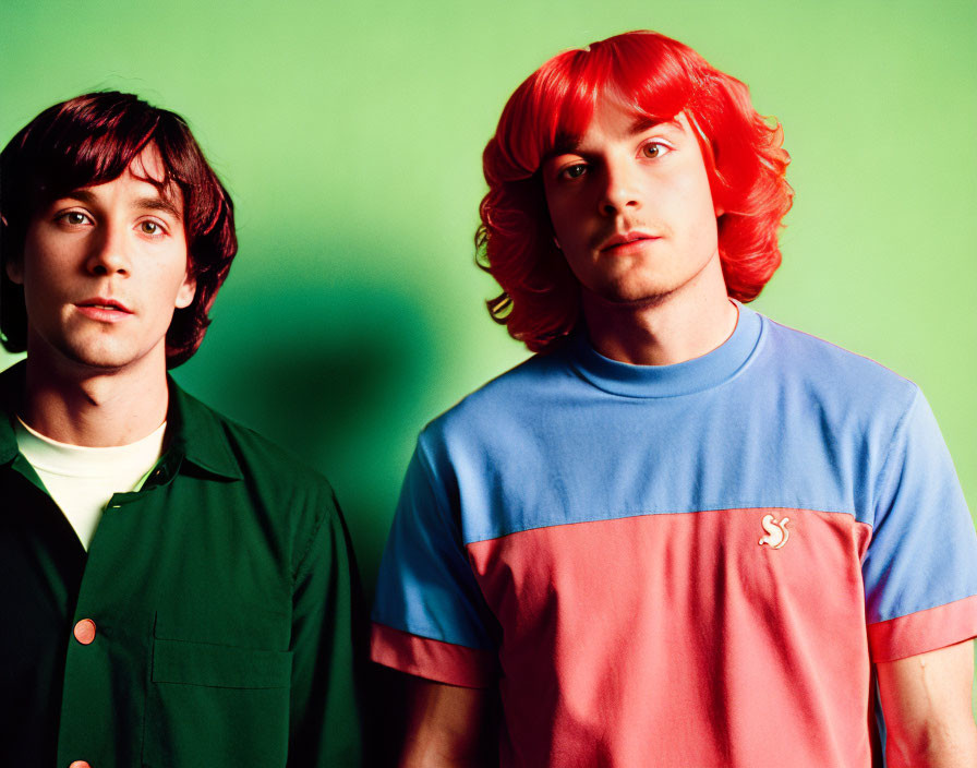 Two men posing in front of green background, one in green shirt and dark hair, the other in