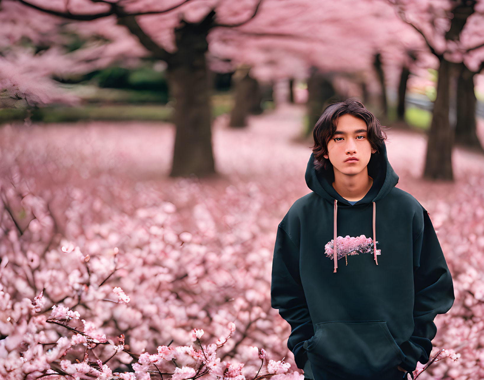 Young person with tousled hair in black hoodie against pink cherry blossoms.