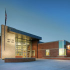 Modern building with large windows in snowy dusk scene with American flag and people outside.