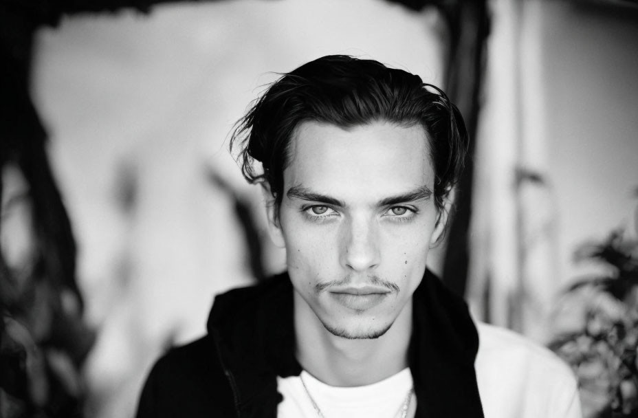 Monochrome portrait of young man with medium-length hair and intense gaze in dark shirt