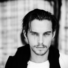 Monochrome portrait of young man with medium-length hair and intense gaze in dark shirt