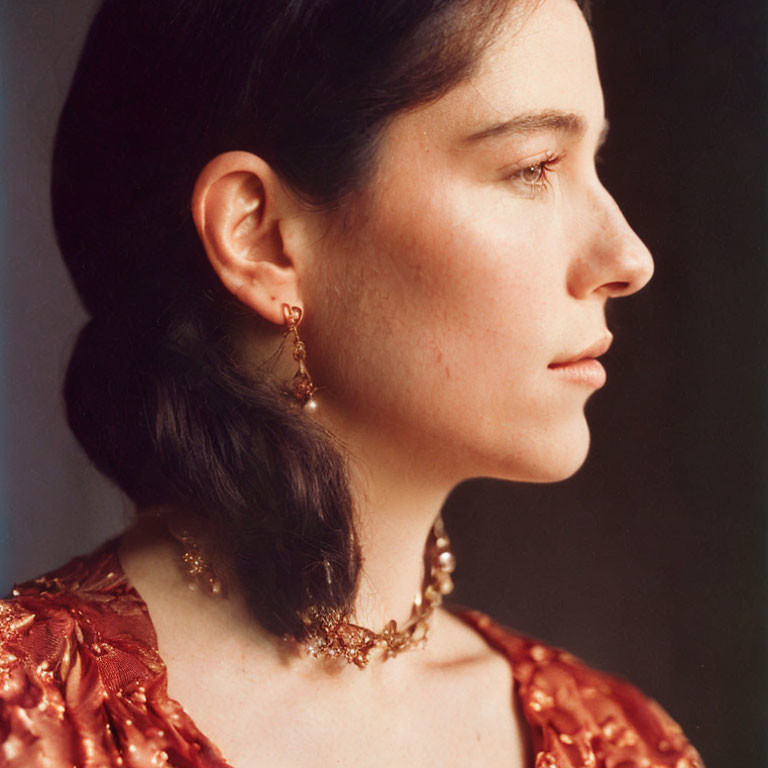 Contemplative woman in red textured top with gold accessories