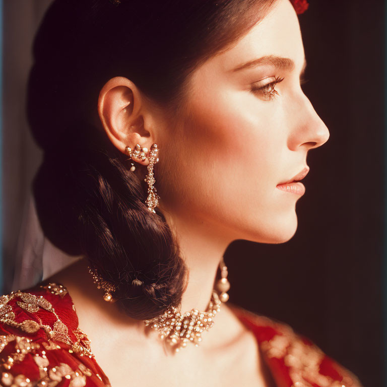 Profile of woman with braided hairstyle in red dress with gold embroidery and ornate gold jewelry.