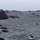 Barren rocky landscape with boulders and distant spire under hazy sky