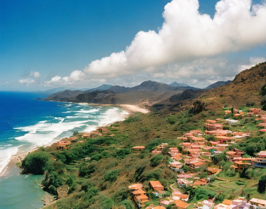 Coastal village with terracotta roofs, mountains, beach, and azure waves