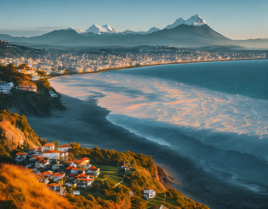 Sunrise coastal landscape: beach, hillside houses, snow-capped mountains