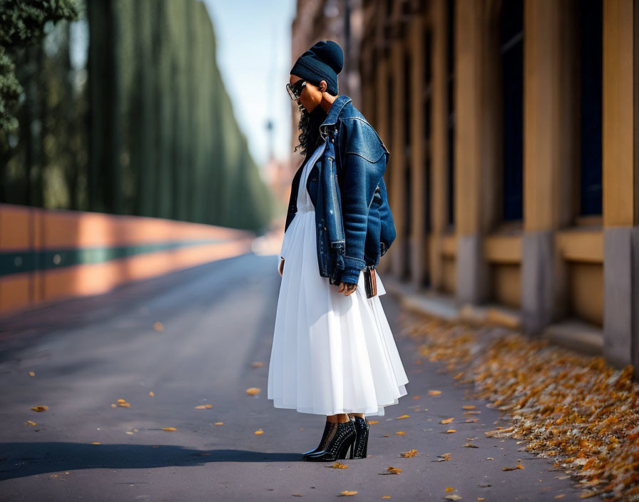 Stylish woman in white skirt and denim jacket on tree-lined street