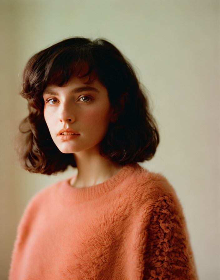 Dark-haired Woman in Bob Haircut Wearing Peach Sweater gazes at Camera