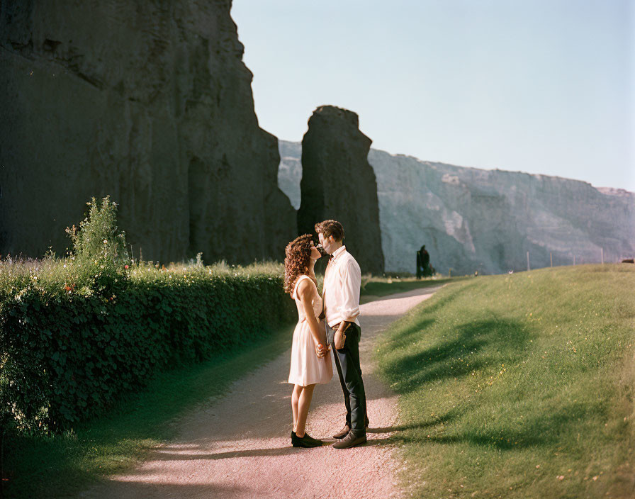 Sunlit pathway with two people facing each other near tall cliffs