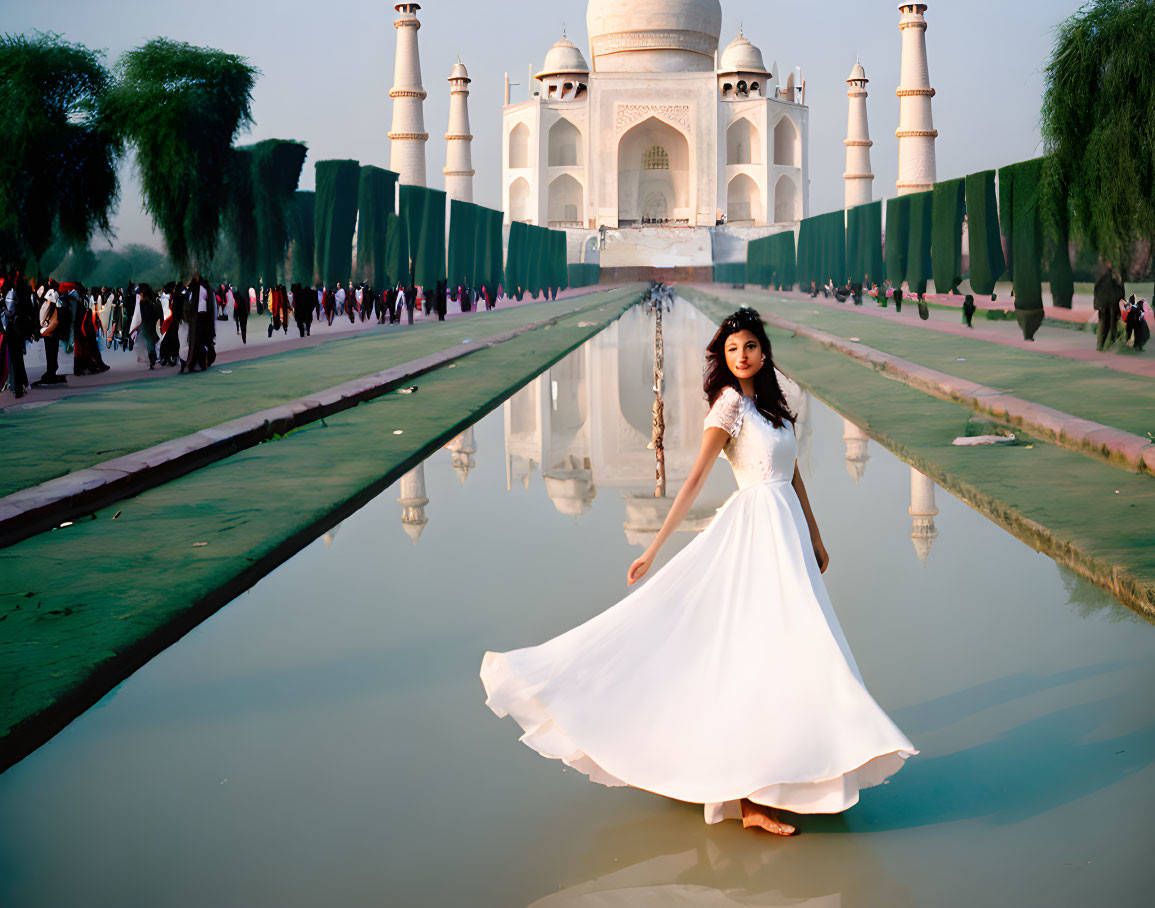 Woman in white dress at Taj Mahal reflecting pool with visitors and clear sky