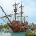 Wooden sailing ship with tall masts and billowing sails in tropical waters.