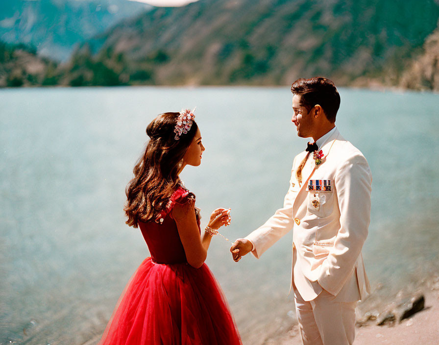 Elegant couple in red and white attire by serene lake and mountains