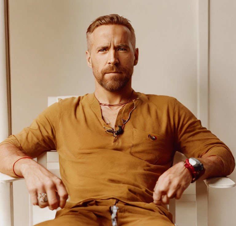 Confident man with neatly trimmed beard in brown attire on creamy background