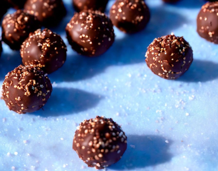 Chocolate truffles with sprinkles on blue surface, one in focus