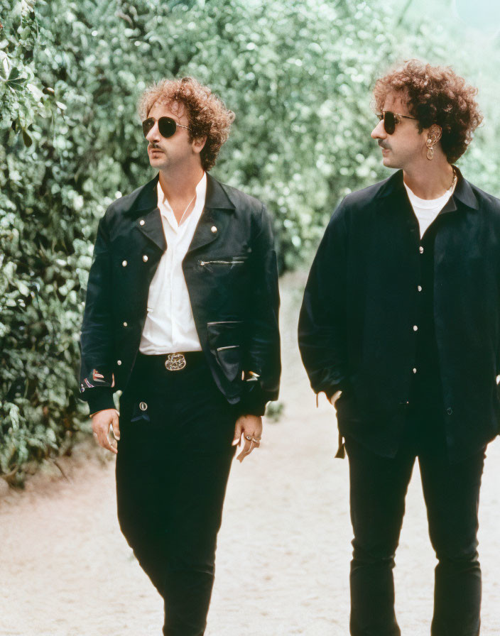 Curly-haired individuals in black attire walking along tree-lined path