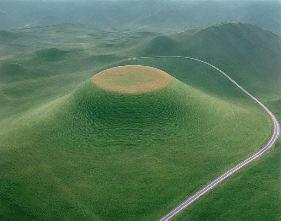 Curving Road Surrounds Green Hill in Rolling Landscape