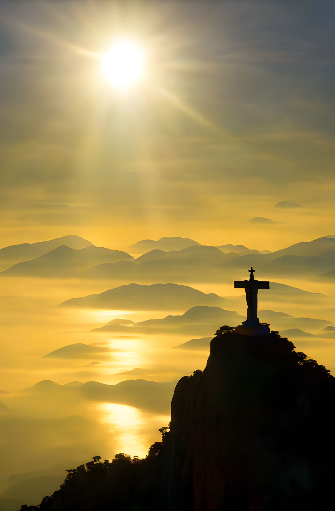 Silhouette of cross on mountain under golden sky with misty mountains.