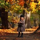 Young girl in coat on tree-lined path with autumn leaves and glowing street lamps