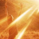 Person with raised arms in warm sunlight in golden forest