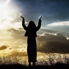 Silhouette of person with raised arms at sunset over wild grassy landscape