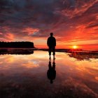 Person's silhouette admiring vibrant sunset over red-clouded water