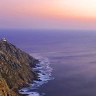 Coastal landscape with house on cliff, rolling hills, and pastel sunset