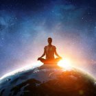 Person meditates in cosmic setting with vibrant starry sky and radiant sunrise.