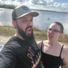 Bearded man in military uniform with woman in black dress by beach and sky