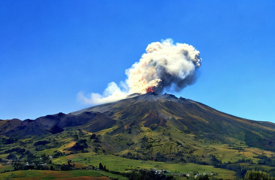 Volcano erupting over green hills with ash and smoke