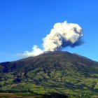 Volcano erupting over green hills with ash and smoke