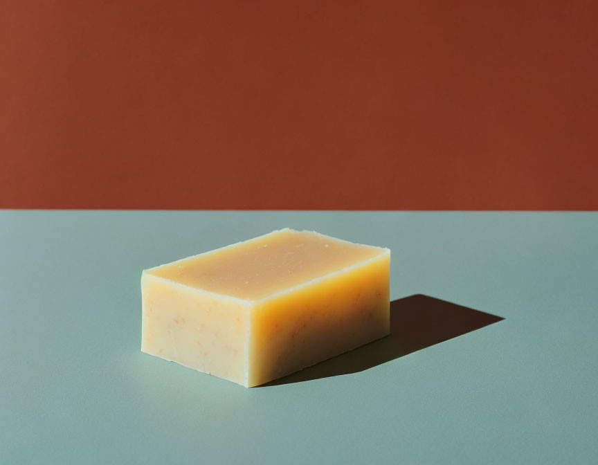 Textured bar of soap on grey countertop with orange background and sharp shadow