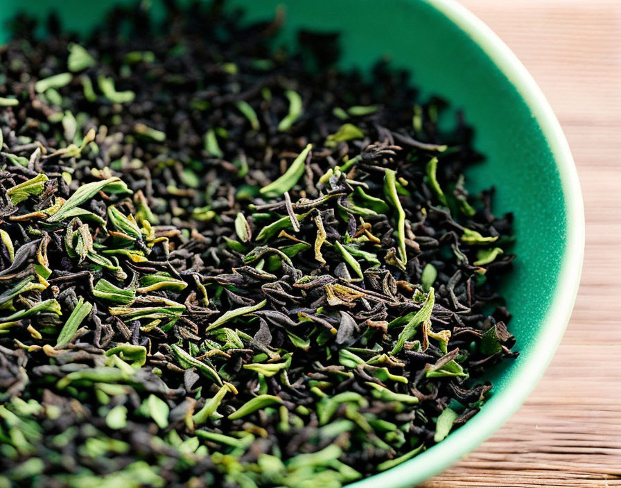 Green dried tea leaves in a bowl on wooden surface