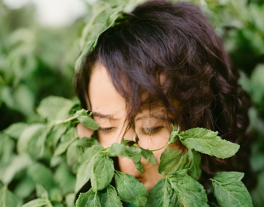 Face partially hidden by lush green leaves, serene expression.