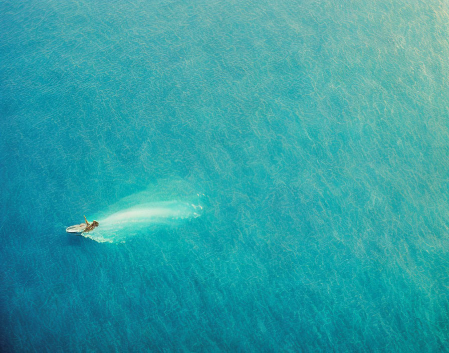 Boat cruising in vast blue ocean with white wake trail