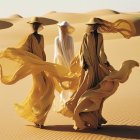 Three women in golden dresses and veils standing in desert breeze