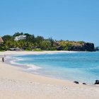 Tranquil beach scene with lone figure, turquoise waters, sandy shore, coastal house, and blue