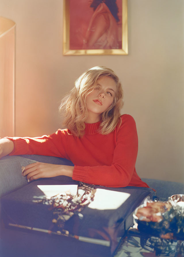 Woman in red top lounging on couch in warm sunlight with vase of flowers