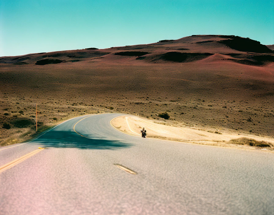 Motorcyclist riding on winding road through arid landscape