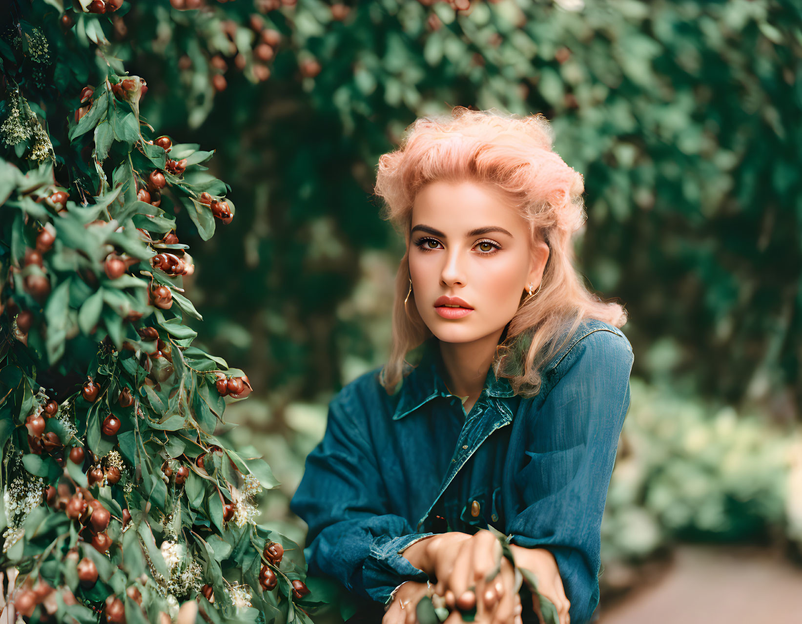 Blonde woman in denim jacket posing in green bushes with red berries