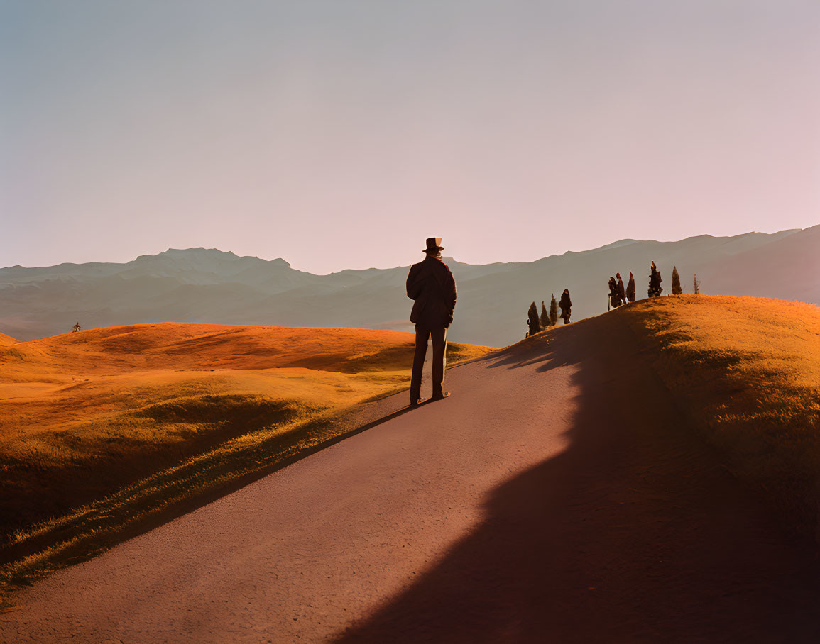 Lonely figure at sunset on winding path with group in distance and rolling hills.