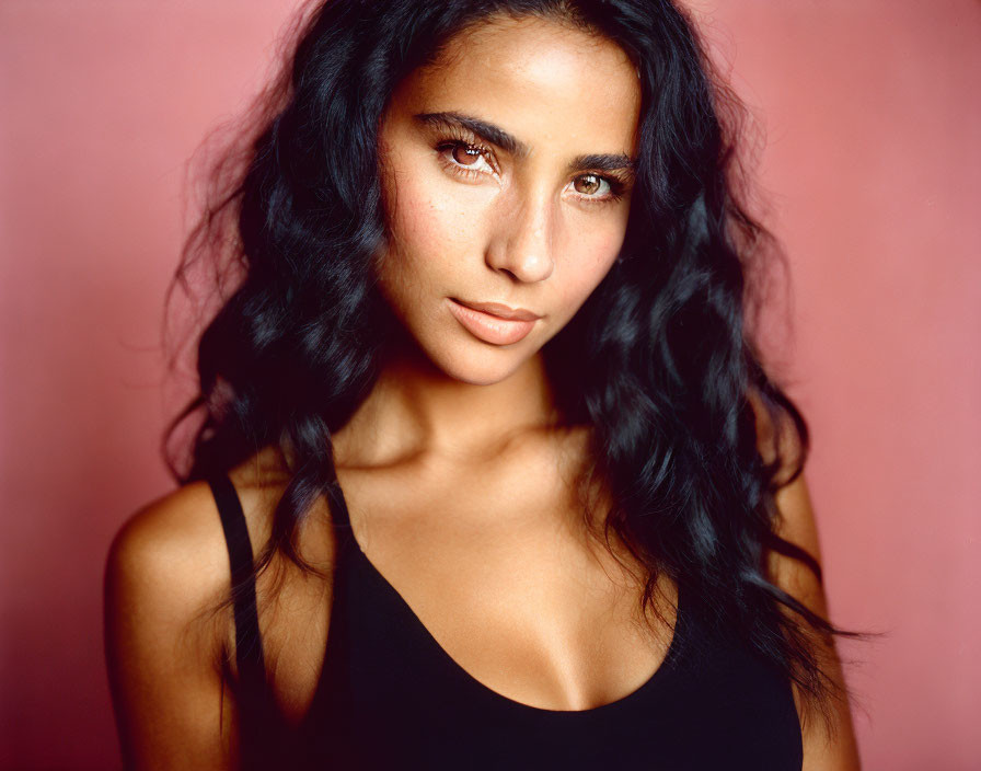 Portrait of Woman with Long Curly Dark Hair and Brown Eyes in Black Top on Pink Background