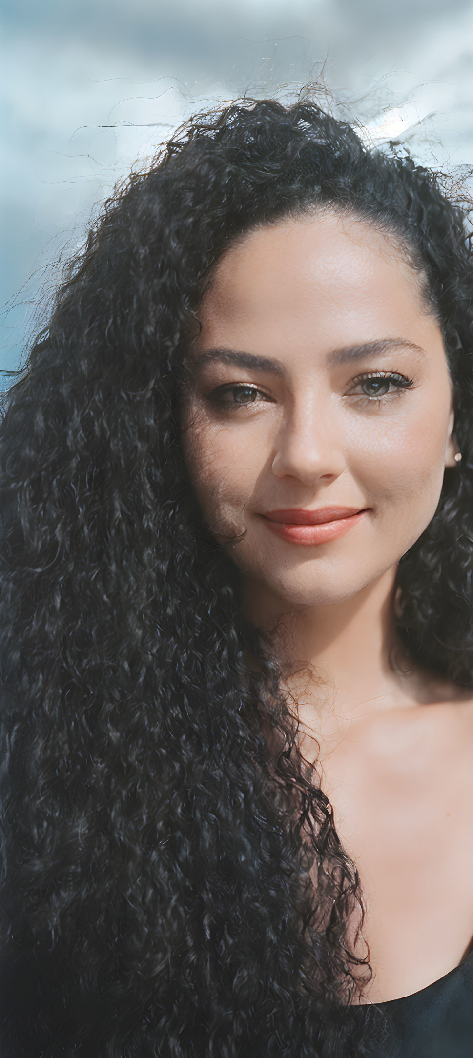 Portrait of Woman with Curly Hair and Subtle Smile against Cloudy Sky