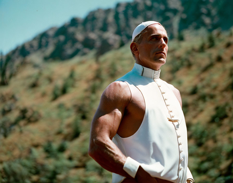 Muscular man in white uniform gazes at mountains