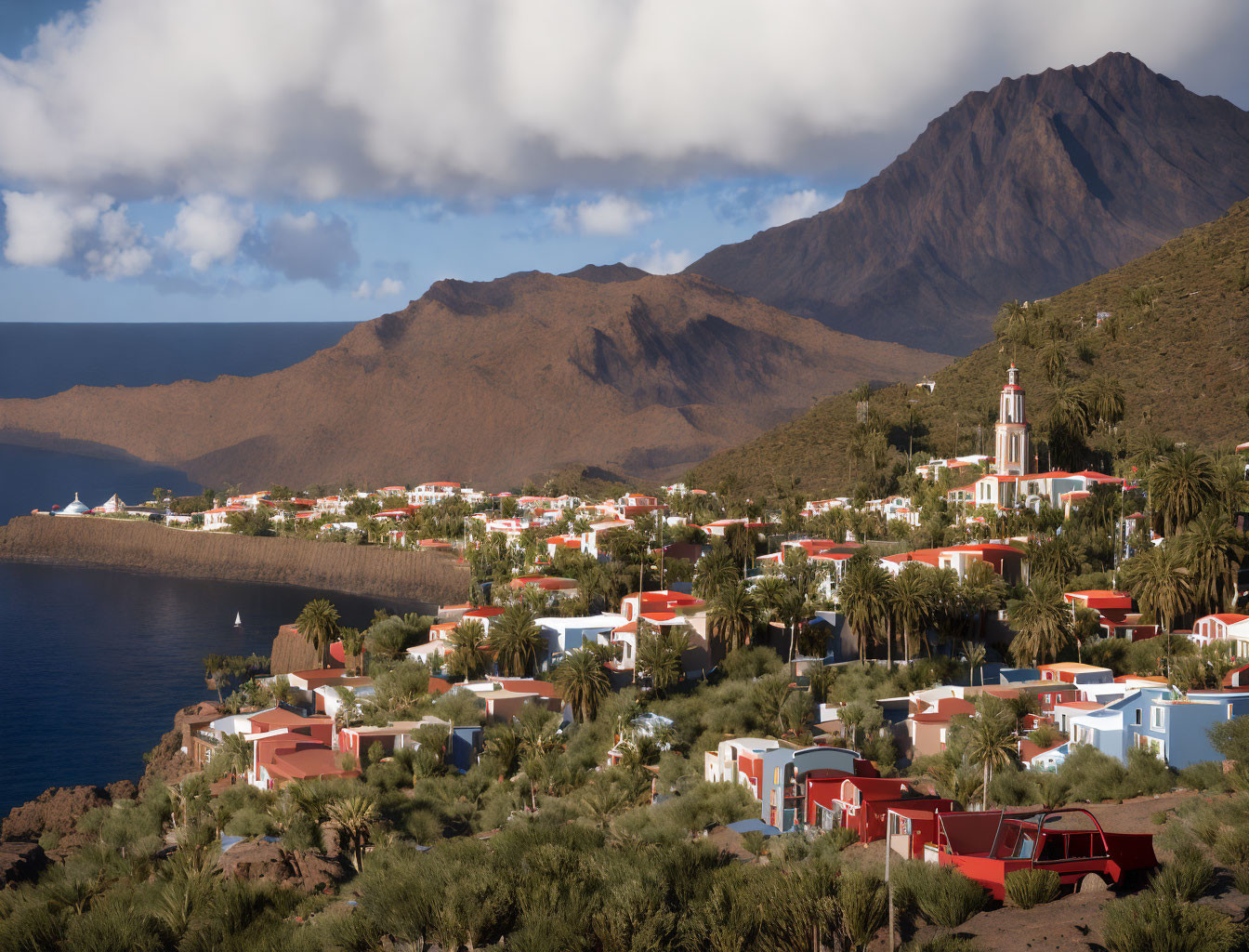 Scenic coastal village with red-roofed buildings and church tower amidst mountains