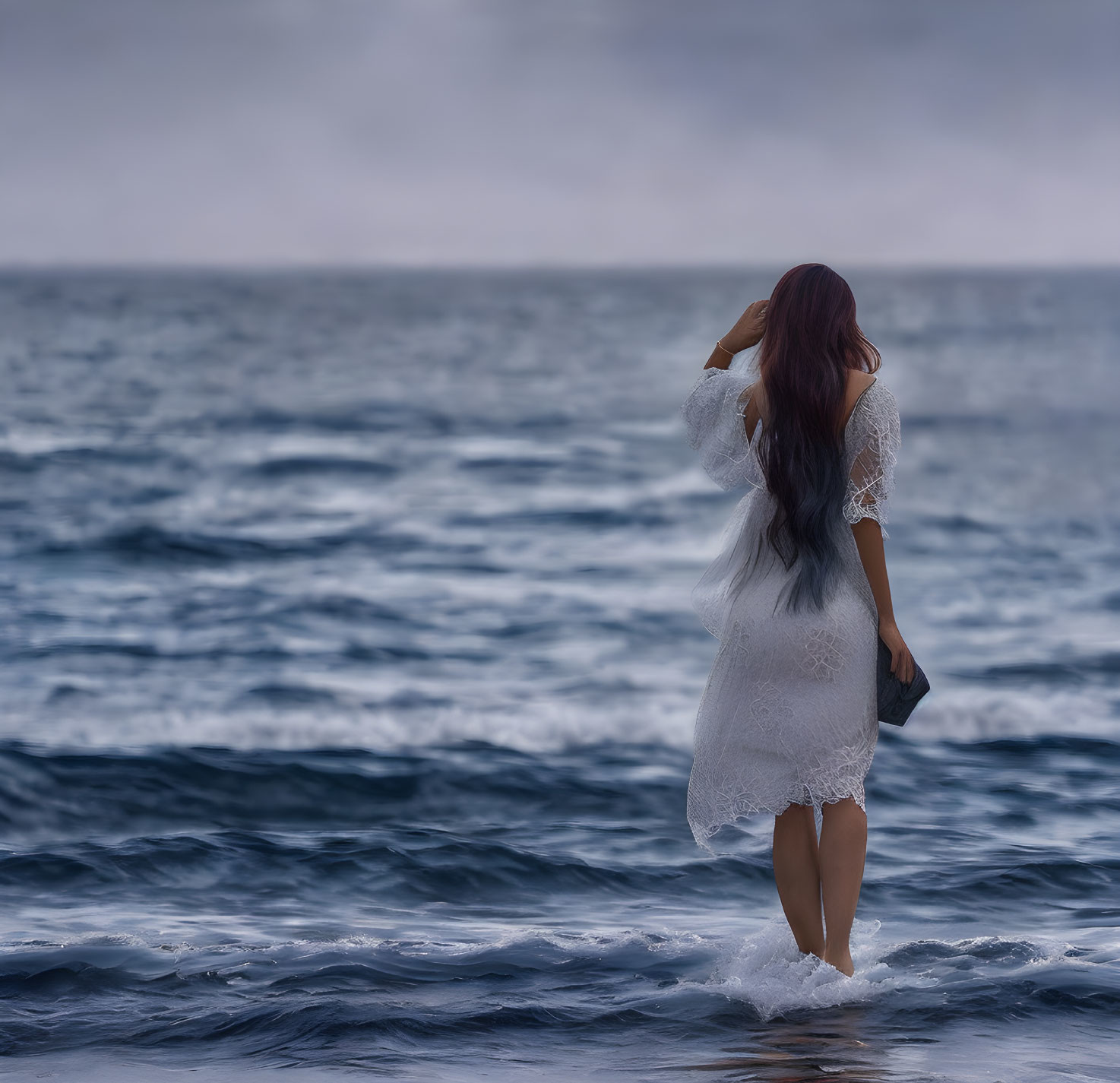 Woman in lace dress standing in ocean under overcast sky