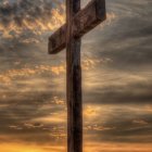 Silhouetted wooden cross at sunset with orange sky and serene landscape